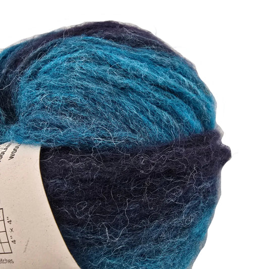 Close-up Image of a single ball of Feeling Good Yarn by Wool And The Gang in the color Northern Lights Green Stripe with label on a white background.