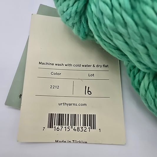 Close-up Image of label on a bulky, cotton yarn by brand Urth Yarns in the color Galatea (which is a bright tonal green) with a white background.