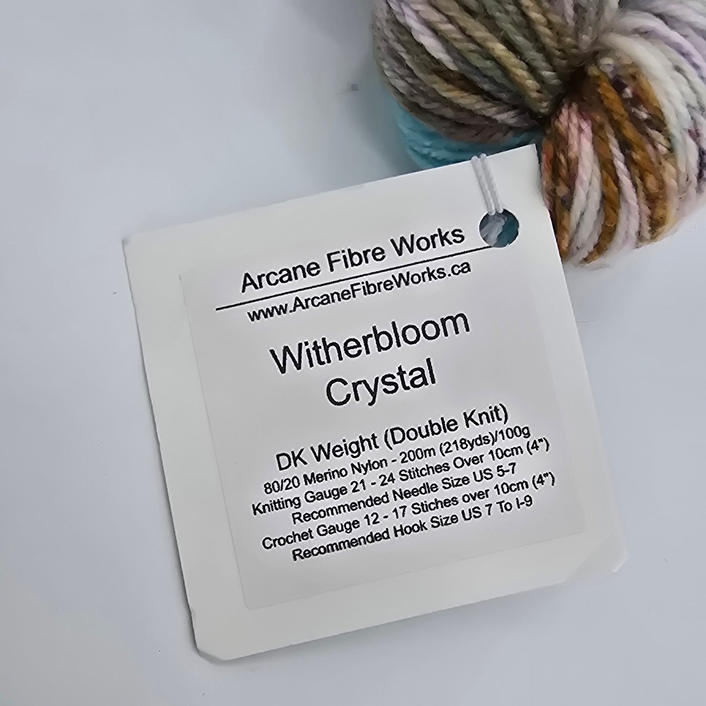Close-up image of label on a single skein of DK Yarn by Arcane Fibre Works on a gray background.