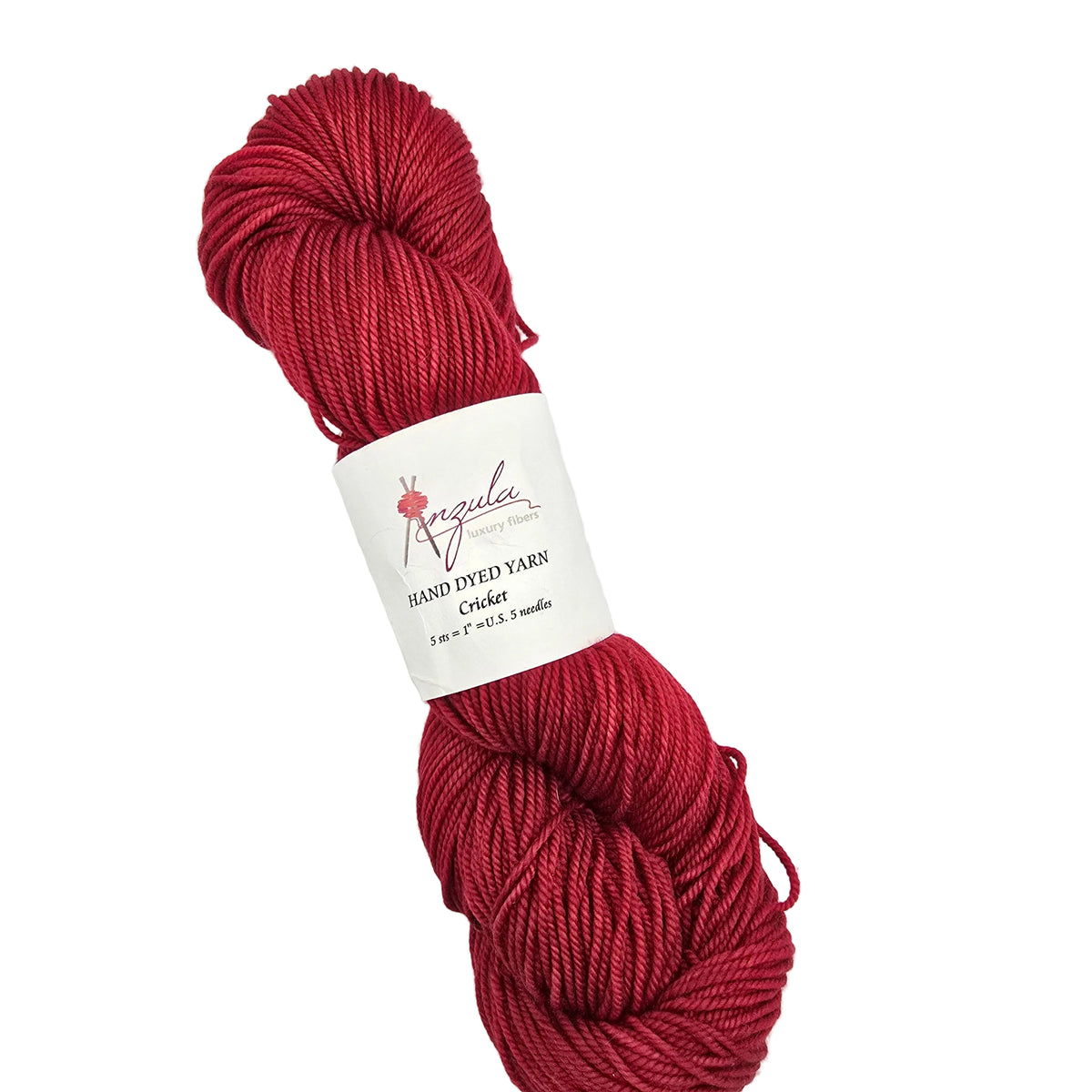 A skein of deep red hand-dyed yarn with a white paper label reading 'Anzula Hand Dyed Yarns' and 'Cricket', photographed on a clean white background.
