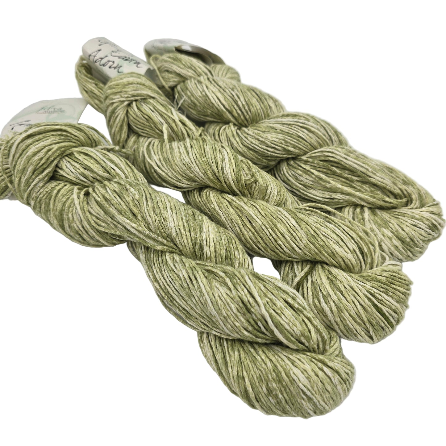 Three skeins of Good Earth Adorn yarn by Fibra Natura in color Lettuce which is a green and white with labels on a white background.