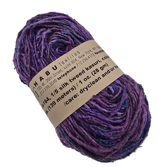 Image of a single skein of A-164 1/5 Silk Tweed Kasuri Yarn by Habu Textiles in  Color L10 with label on a white background.