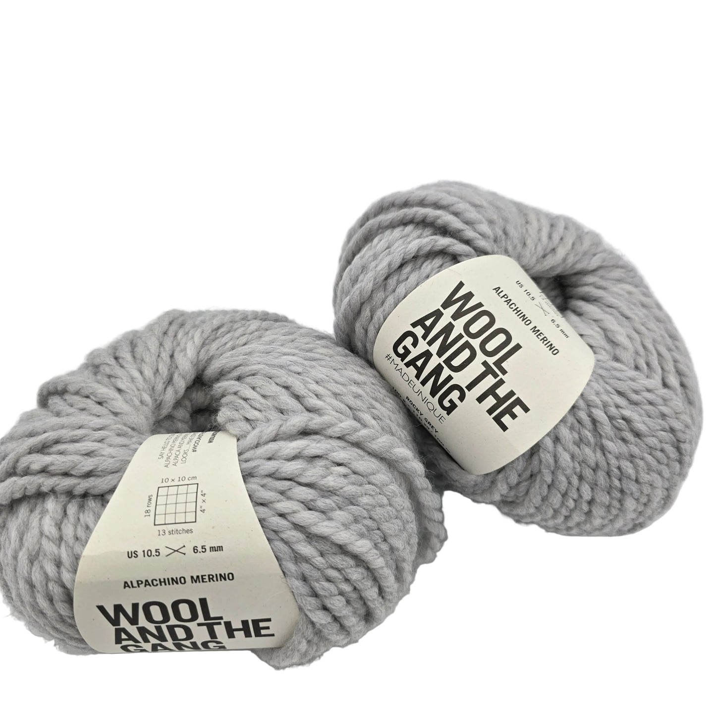 Image of two balls of Alpachino Merino by Wool And The Gang Yarn in the color  Rocky Grey with labels on a white background.