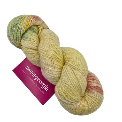 A skein of variegated yarn in soft pastel shades of pale yellow, mint green, and dusty pink, with a magenta paper label reading 'sweetgeorgia' on a plain white background