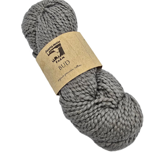 A skein of BUD_yarn by_Juniper_Moon_Farm_in_Color_101 chunky gray yarn wrapped in a kraft paper label on a white background.