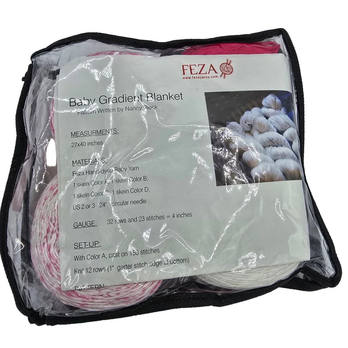 A packaged baby gradient blanket pattern kit by Feza on a white background. The kit is sealed in a clear plastic bag with a black zipper, containing yarn balls in pink, red, and white, along with an instruction card detailing measurements, materials, and setup instructions.
