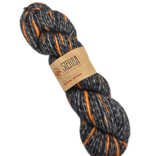 A skein of Baby_Pima_yarn by_Sierra_-in the color Dark_Charcoal a heathered charcoal gray and balck colorway with bright orange stripes with wrapper on a white background.