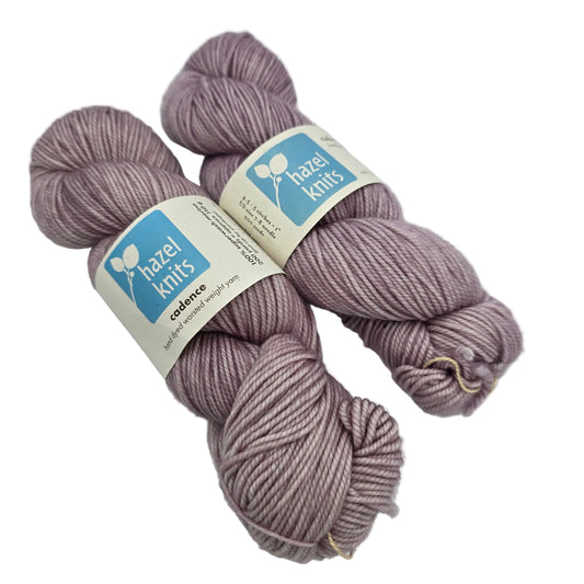 image of two skeins of Cadence yarn by Hazel Knits in the color thistle with labels on a white background.