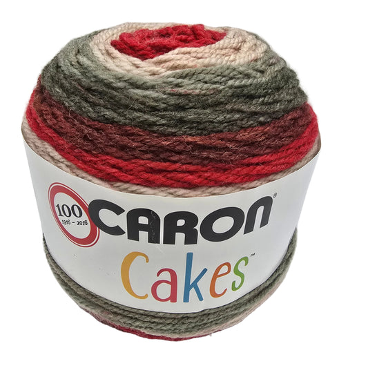 A cake of Caron Cakes yarn with a variegated pattern of red, olive green, brown, and cream, wrapped in a white paper label.