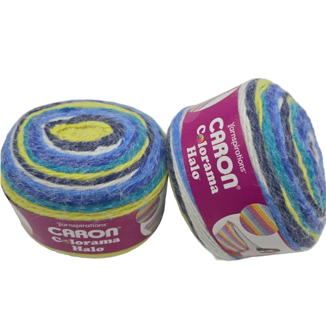 Two skeins of Caron Colorama Halo yarn  in the color Splash a Bluem White and green yarn on a white background. One skein is upright, showing a purple label, and the other is lying on its side, showing the variegated yarn texture.