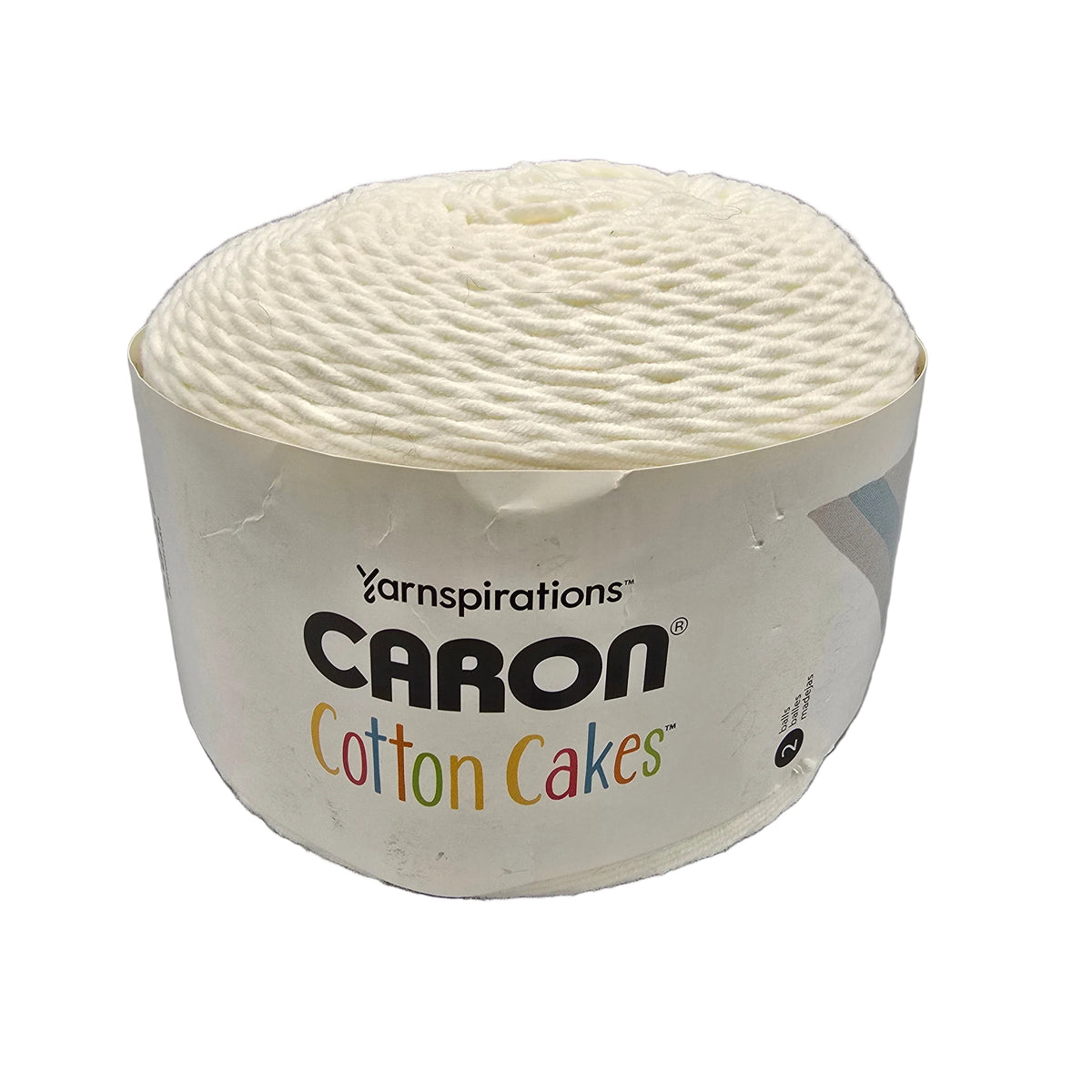 A large spool of Caron Cotton Cakes yarn in a warm off-white/cream shade, shown on a white background. The paper label clearly displays the brand 'Yarnspirations' and 'CARON'.