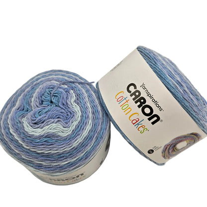 Image of two cakes of Caron Cotton Cakes Yarn in the color Wild Blueberry with labels on a white background.