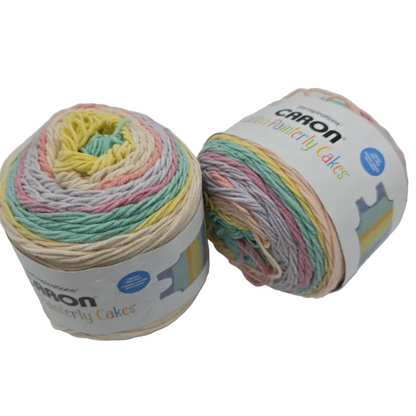 Image of two cakes of Caron Cotton Painterly Cakes Yarn in the color Coral Cascade with labels on a white background.