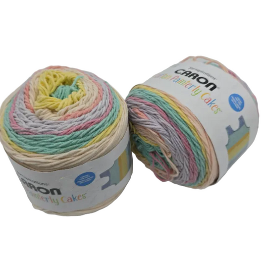 Image of two cakes of Caron Cotton Painterly Cakes Yarn in the color Coral Cascade with labels on a white background.