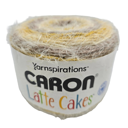 Image of a single cake of Caron Latte Cakes  Yarn in the color Butter Cookie with label on a white background.