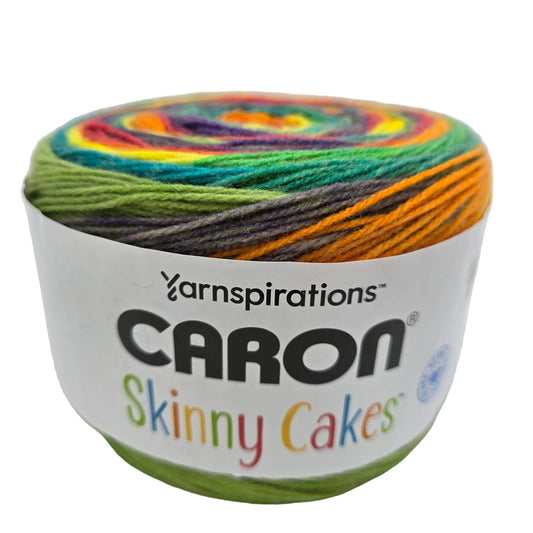Image of a single skein of Caron Skinny Cakes yarn in the color Rainbow with label on a white background.