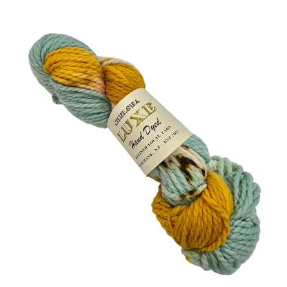A skein of  Chunky Yarn by Chelsea Luxe  in the color I Love NY a variegated yarn with sections of pale mint green and mustard yellow, wrapped in a cream paper label that reads 'LUXE Mixed Yarn' on a white background.