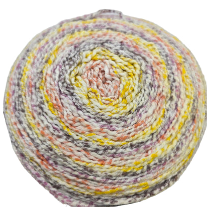 Close-up image of single cake of Caron Cotton Ripple Cakes yarn in the color  Mauve Glow on a white background.