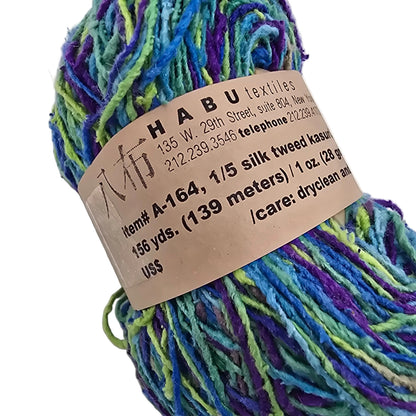 Close-up Image of a single hank of A-164 1/5 Silk Tweed Kasuri Yarn by Habu Textiles in the Color L9 with label on a white background.
