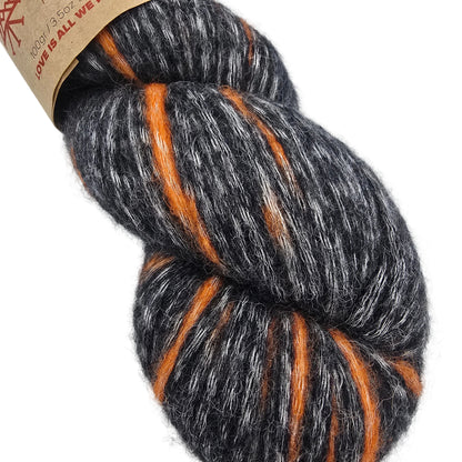 A close-up of a skein of fuzzy yarn with a heathered dark gray and white base and bright orange stripes,