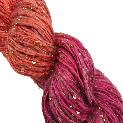 A close-up of Beaded_Rhapsody_Sequins_Yarn_by_ArtYarns_in_Color_115_Gold a yarn transitioning from coral orange to deep magenta, with small scattered gold sequins embedded throughout, set against a plain white background.