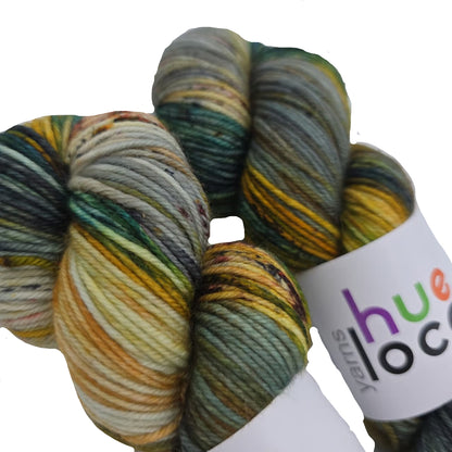 Close-up image of two skeins of DK by Hue Loco yarn in the color  Serama Rooster with partial label on a white background.