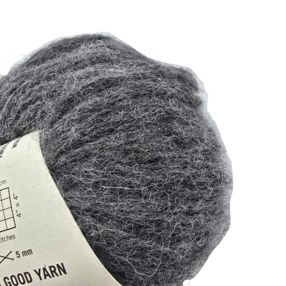 Close-up Image of a single ball of Feeling Good Yarn by Wool And The Gang in the color Silver Fox Grey with partial label visible on a white background.