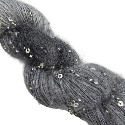 A close-up image of Mohair Splash yarn by ArtYarns  in color 148 Silver which is a gray ombre yarn with silver sequins, featuring a white paper label at the top, photographed on a white background.