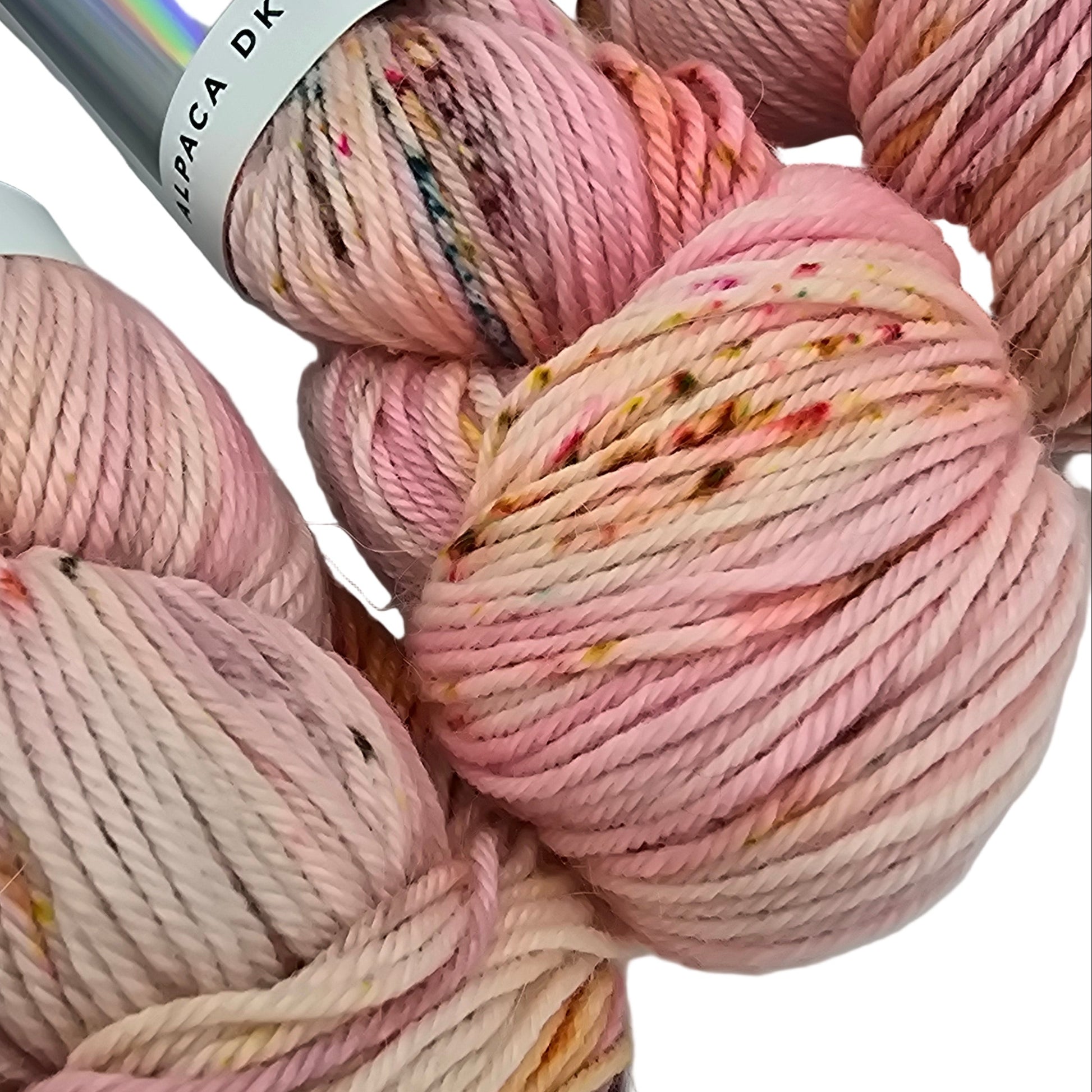 Close-up image of mage of skeins of Alpaca DK yarn by the brand hedgehog in the color Taffy (which is multiciolor with a light pink base with brown, grey, and orange) with labels on a white background.