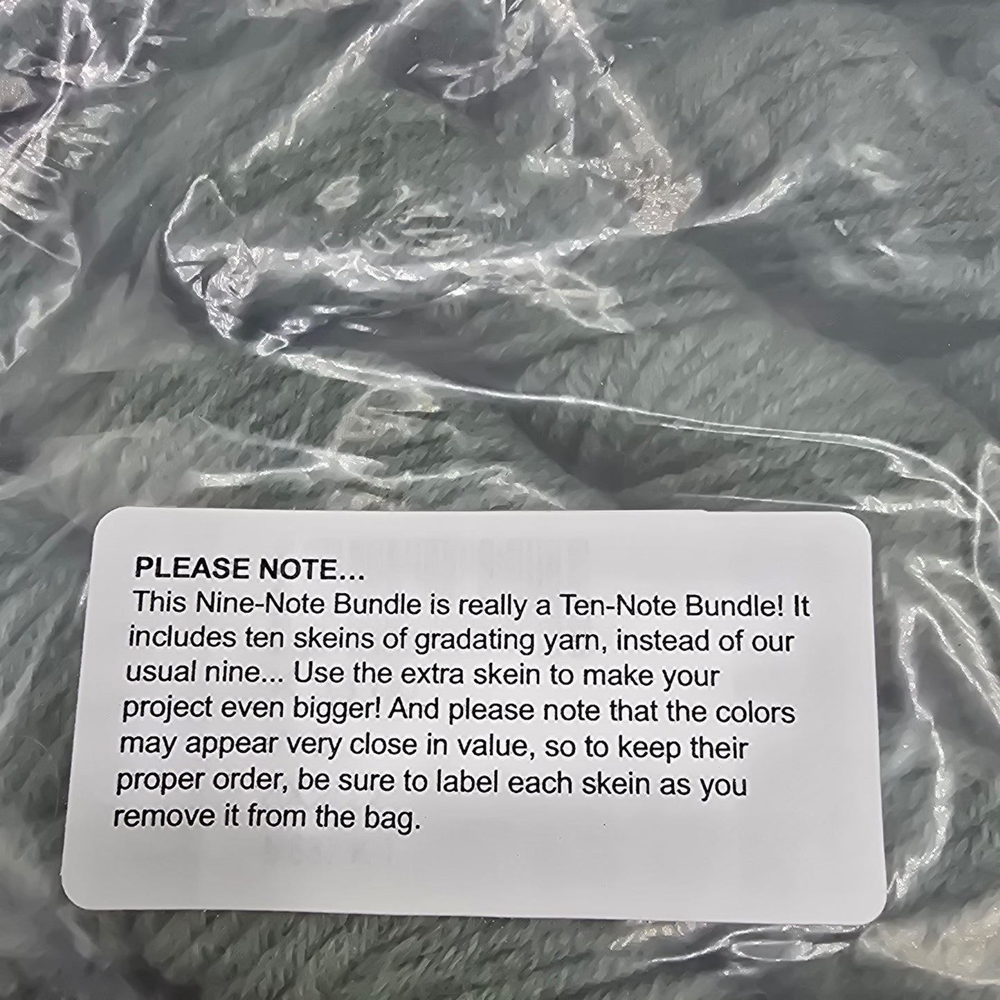 Close-up image of label on a bundle of 10 skeins of yarn in a gradient from light to dark green in a color called juniper by the brand purl soho no background visible.
