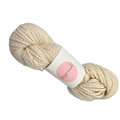 A skein of Cloud_Bulky_yarn by_Little_Wing_Fibers in the color Onigiri a cream-colored  yarn with  a label on a white background.