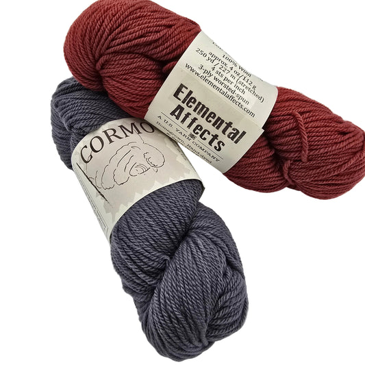 Two skeins of yarn on a white background: one rust red and one slate gray, both with paper labels. The top label reads Elemental Affects and the bottom label reads CORMO.