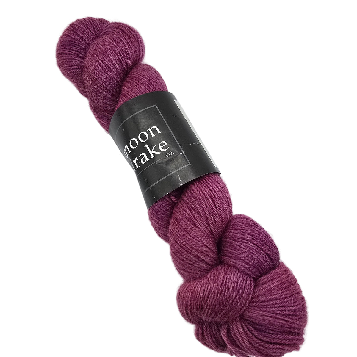 A skein of Corridale Fingering Yarn by Moon Drake Co. in the color Leftover wine a deep berry purple shade, wrapped with a black paper label on a white background.