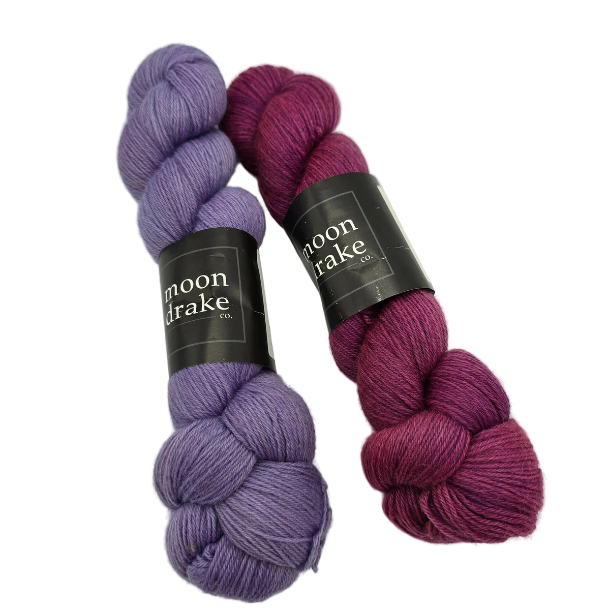 Two Skeins of Corriedale_Fingering_yarn by_Moondrake_Co.with labels on a white background.