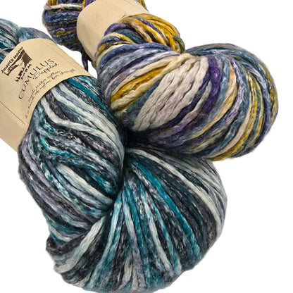 Image of two skeins of Cumulus Dappled  Yarn by Juniper Moon Farm in variegated blues and purples with labels on a white background.
