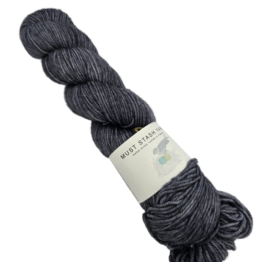 Image of a single skein of DK Tonal Yarn by Must Stash Yarn in the color Night Owl with label on a white background.