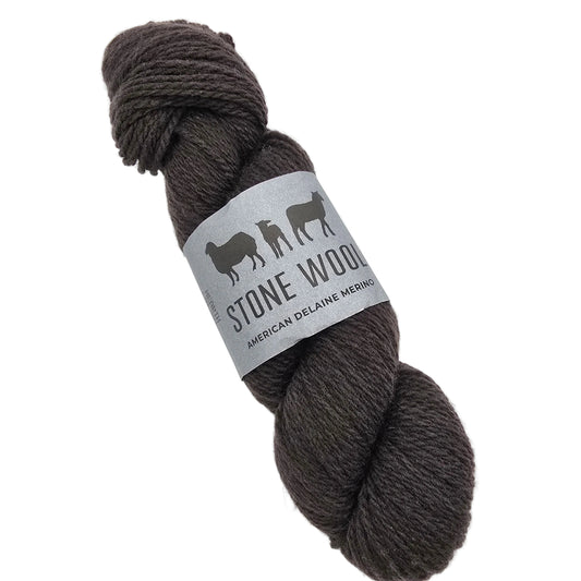A skein of Stone Wool yarn in a dark grey-brown color, featuring a gray paper label with black sheep silhouettes and the text 'STONE WOOL' and 'AMERICAN DELAINE MERINO', set against a plain white background.