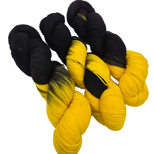 image of three skeins of black and yellow yarn by Frolicking Feet in color Team Spirit on a white background.