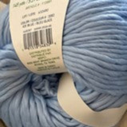 A close-up of light blue yarn with a white paper label showing a barcode and product details.