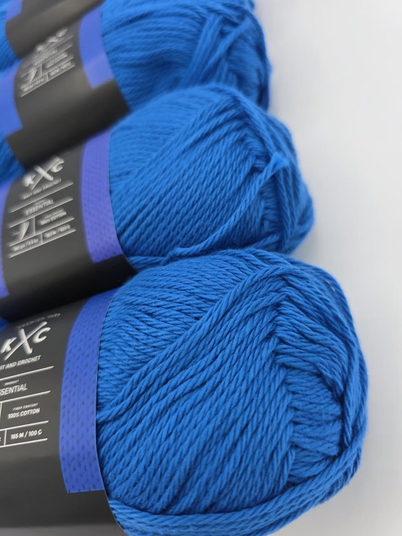 Close-up image of multiple bright blue skeins of K+C yarn with labels on a white background.