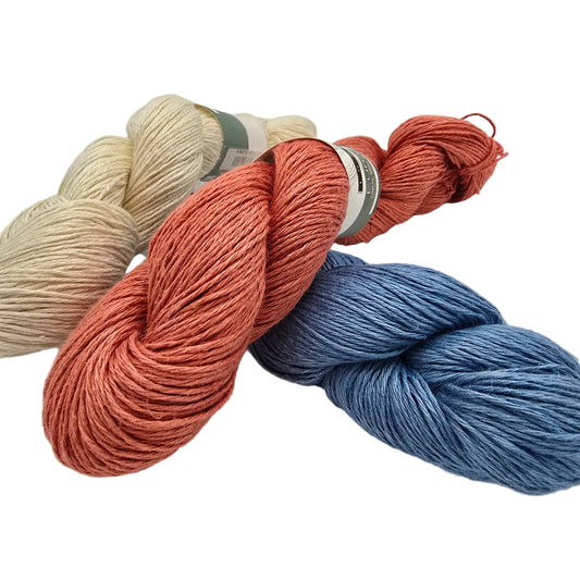 Three skeins of yarn arranged on a white background: one cream/off-white, one coral-orange, and one dusty blue. Each skein has a paper label wrapped around it.
