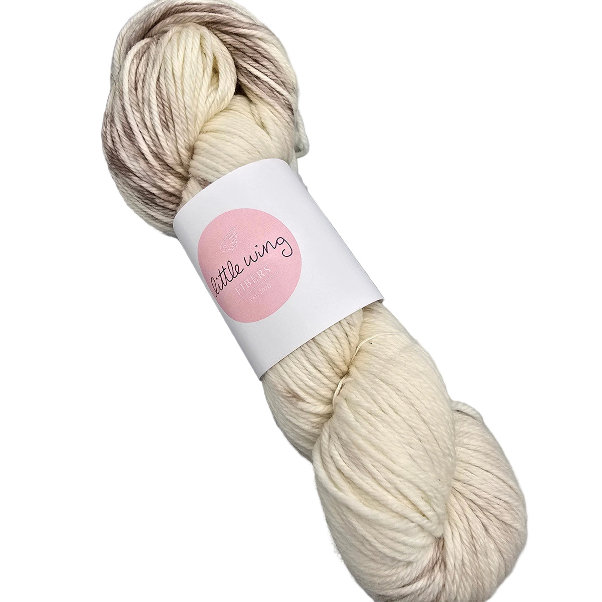 A skein of Featherlight_DK_yarn by_Little_Wing_Fibers in the color Pre-Bake a variegated yarn in cream, beige, and light brown tones, wrapped in a white paper band with a pink circle logo on a white background.