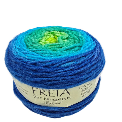A ball of Freia Fine Handpaints yarn with a gradient of colors transitioning from bright lime green in the center, through teal and aqua, to deep royal blue. The yarn is wrapped in a white paper label with the brand name 'FREIA' clearly visible, set against a plain white background.