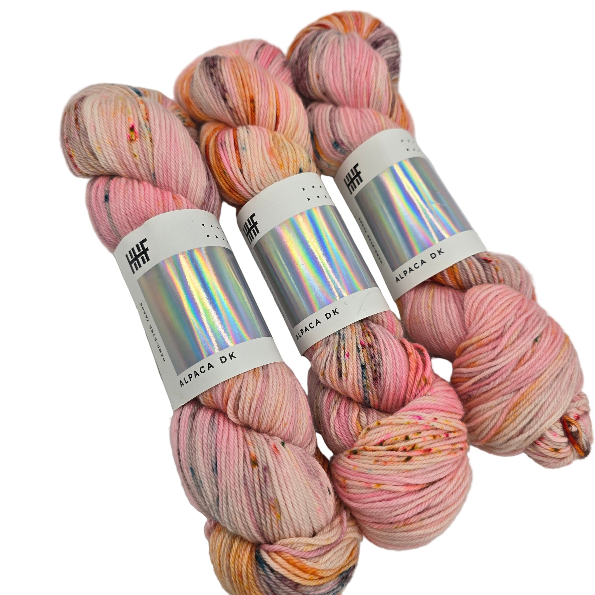 Image of three skeins of Alpaca DK yarn by the brand hedgehog in the color Taffy (which is multiciolor with a light pink base with brown, grey, and orange) with labels on a white background.