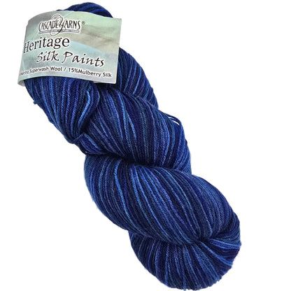 A skein of Heritage Silk Paints yarn,  in the color Deep Water featuring variegated blue and navy tones, with its paper label visible on the left side against a plain white background.
