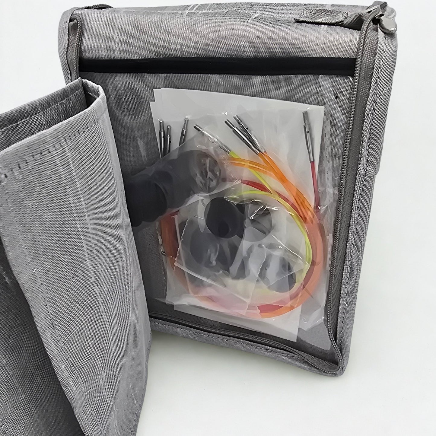 Gray fabric bag with clear window showing knitting needle kit contents on a light gray background
