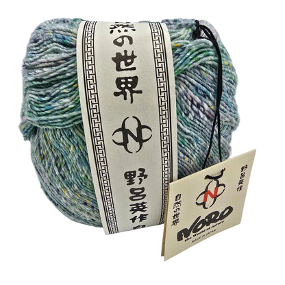 A ball of variegated Kakigori_Yarn_by_Noro  with a cream paper label wrapped around it, alongside a smaller hanging tag. The yarn has a marled texture in shades of mint green, teal, blue, and hints of yellow.