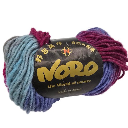 A skein of  Kureyon_by_Noro_in Color_437 a variegated yarn with blue, purple, and magenta sections, wrapped in a black paper label on a white label.