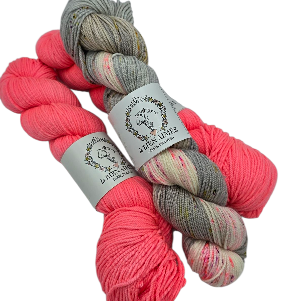 Image of three skeins of La Bien Aimee Yarn, all with labels, on a white background. Two skeins are Salmon Pink and one is Fiori, multicolor gray and pink. Shown as an example of colors that pair will together.