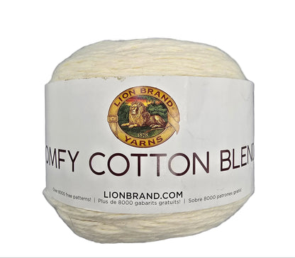 A ball of cream-colored yarn with a white paper label that reads 'COMFY COTTON BLEND' and features the Lion Brand Yarns logo, set against a plain gray background.